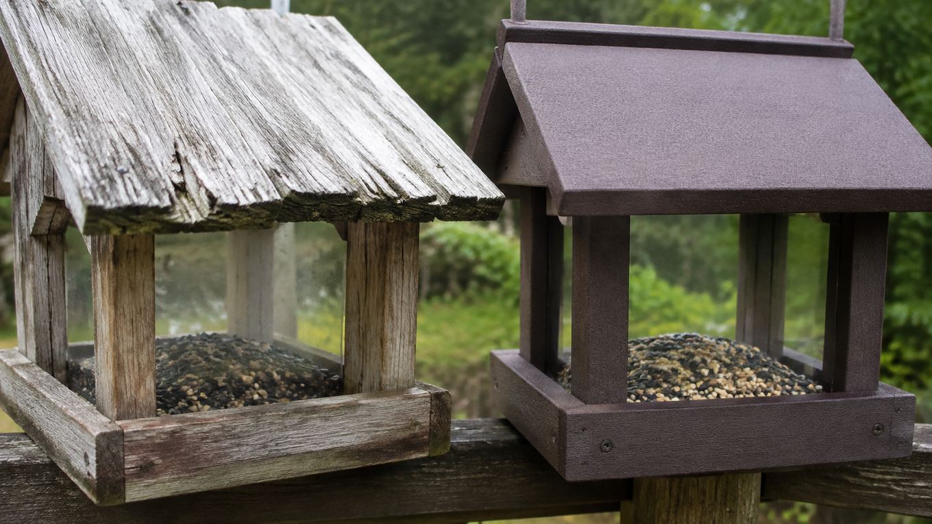A weathered cracked wooden feeder next to a still-vibrant recycled poly-lumber feeder